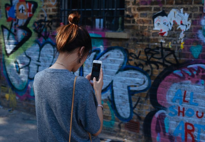 A person taking a photo of a graffiti-covered wall using a mobile phone.