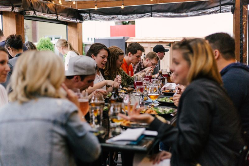 A group of people at a rectangular dinner table eating and talking. 