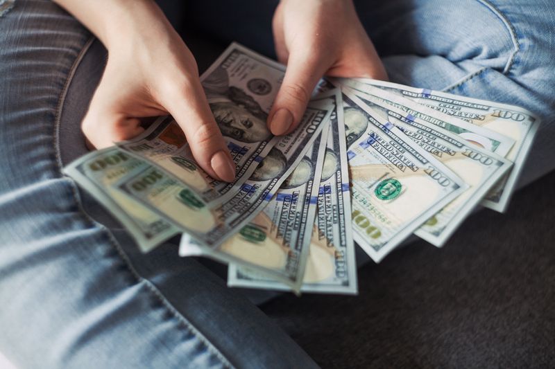 Close up photo of a person's hands holding hundred dollar bills fanned out.