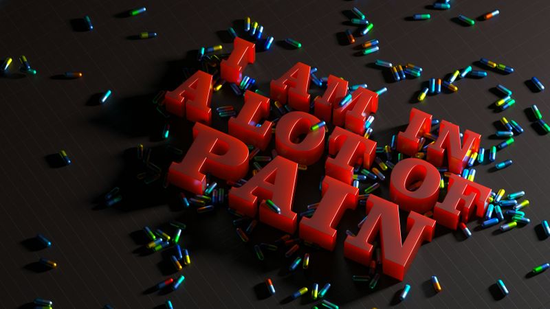 A 3D image reading: 'I am in a lot of pain' surrounded by pills.