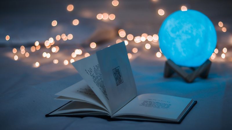 Open book in front of a blue new age crystal lamp and fairy lights.