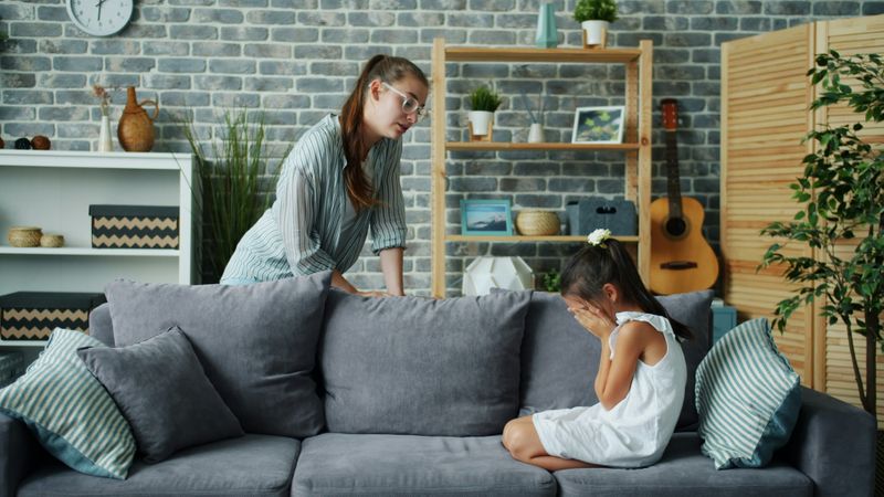 A little girl sitting on a couch while a young woman tries to console her.