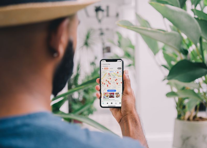 Image of man holding up mobile phone with several pins on map.