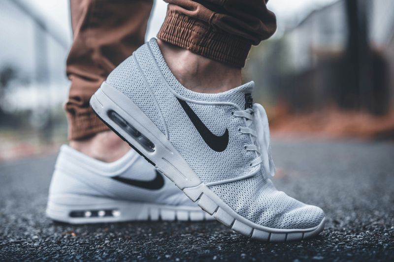 A man wearing a white-greyish shoe with the black Nike swoosh logo.