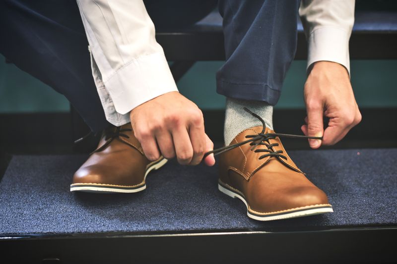 Cropped image of persons' legs and feet. Person tying shoelaces of business casual shoes.