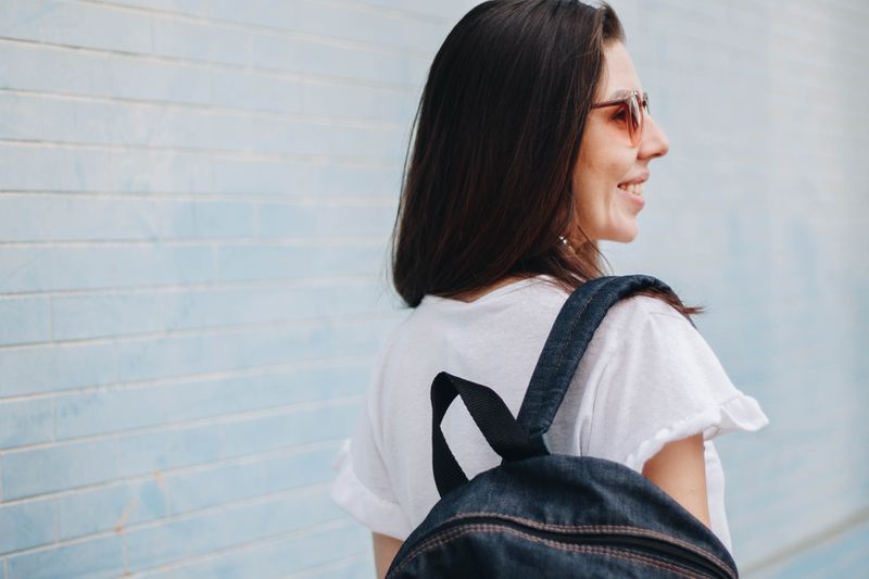 A smiling college student facing away from the camera with a backpack slung on one shoulder.