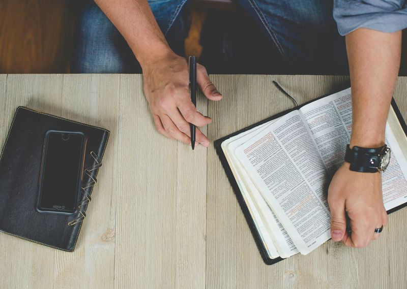 A person sitting at a desk with books, phone, and a pen in hand.