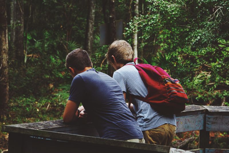 Two young people lean on boardwalk railing in the woods