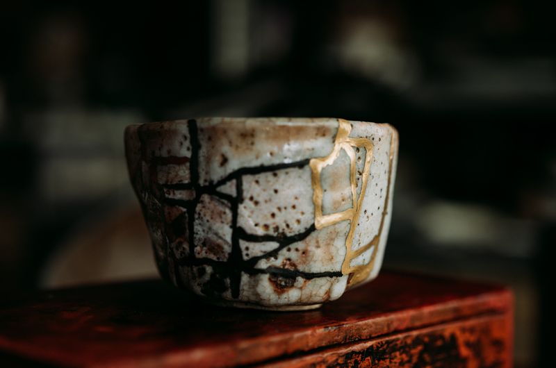 kintsugi cup photo, gold and black threads, imperfect shape yet elegant and beautiful