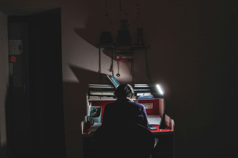 A woman studies at a desk in a dimly lit room.