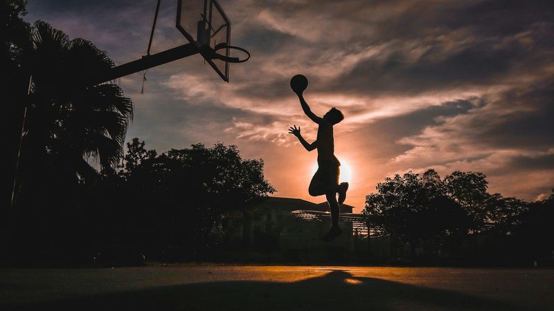 A person holding a basketball, jumping towards the rim of a basketball hoop.