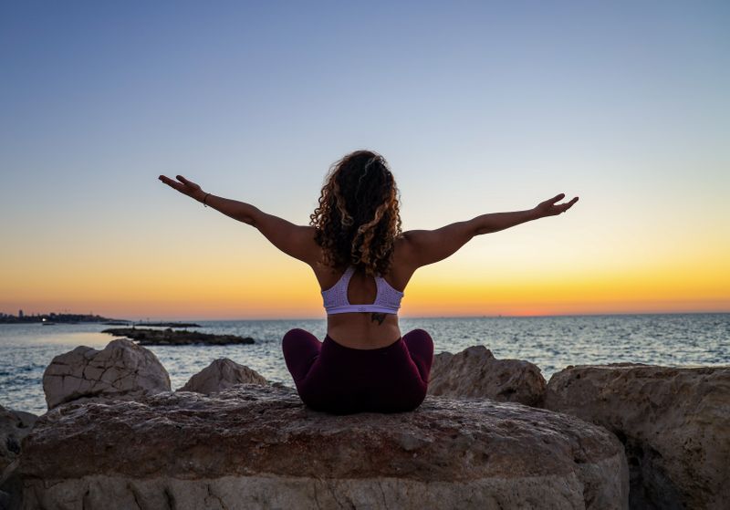 A woman doing yoga on a rock overlooking a bay at sunset.