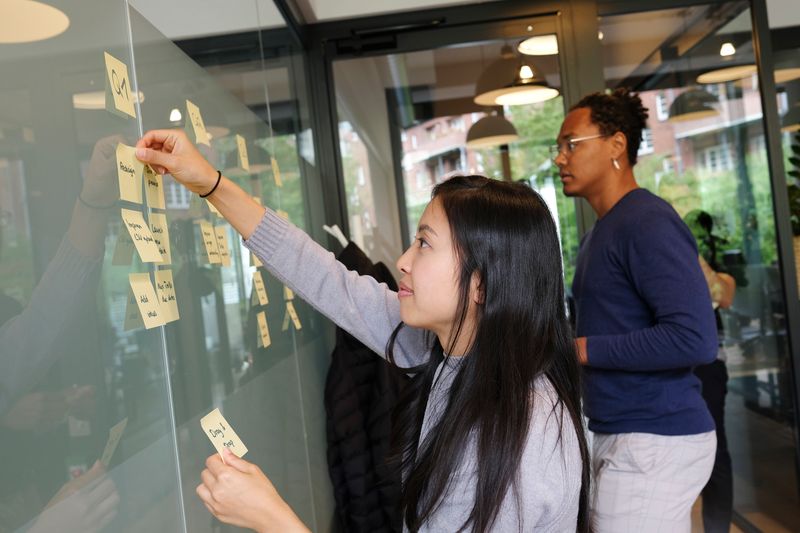 Two people sticking sticky notes on a wall.