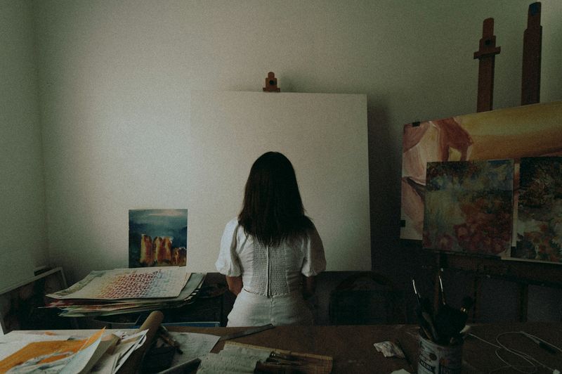 Young woman facing a blank canvas in a room filled with paintings
