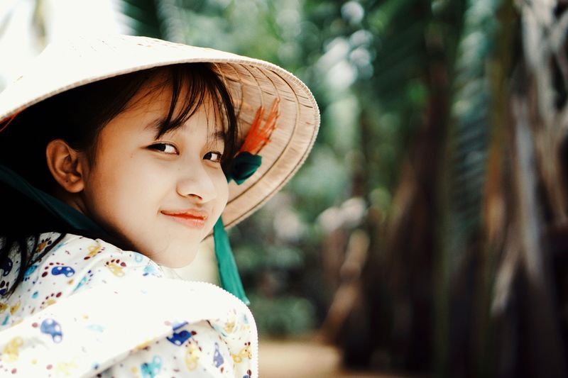 A smiling Vietnamese girl wearing a sun hat.