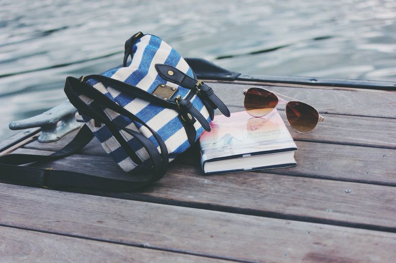A beach bag, book, and sunglasses on a wooden pier.