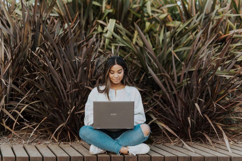 A woman sitting outside with her laptop.