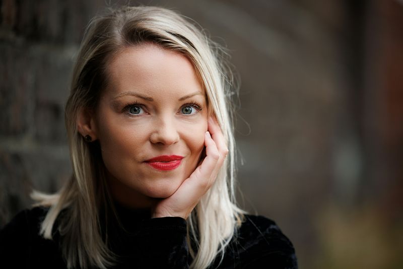 A white woman with a confident, interested expression looking at the camera with her chin resting slightly on one hand.