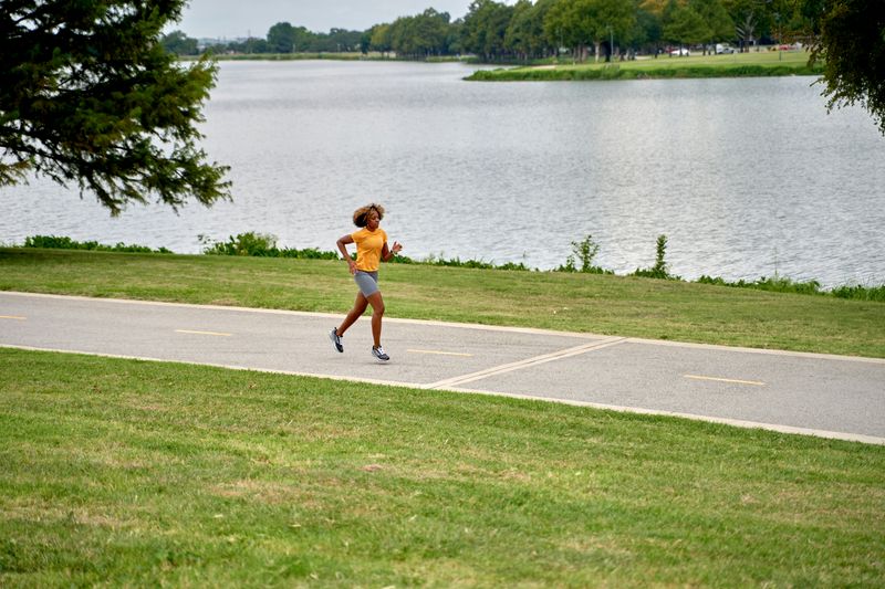 A woman runs on a paved track by the water.