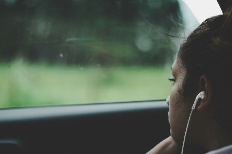 A teen sits quietly in a car, looking out the window with a thoughtful expression.