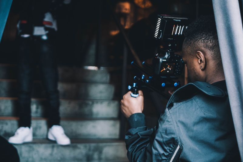 A man holding a camera and shooting an image of a person standing on a staircase.