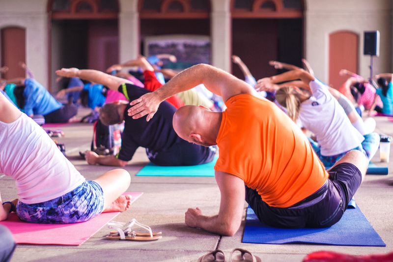 people practicing yoga, sitting cross-legged, leaning on their left elbow and stretching their right arm over to the left