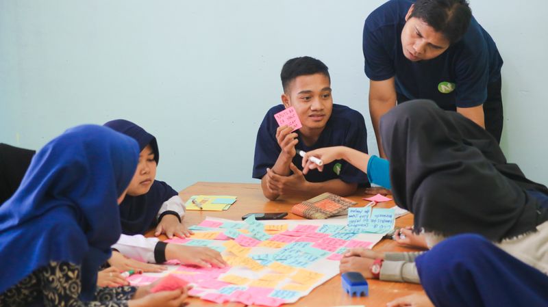 A group of mixed gender schoolchildren work on a project as the teacher assists. They are all actively engaged in the work.