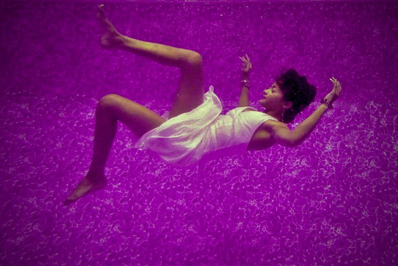 Image: person in white dress floating in purple water.