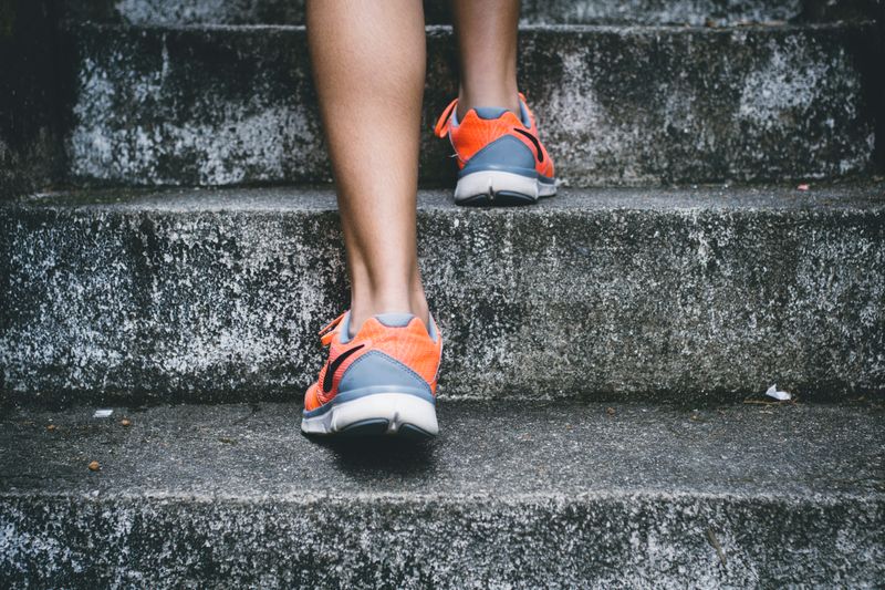 Close up photo of a person's calves and athletic shoes as they walk or fun up concrete steps.
