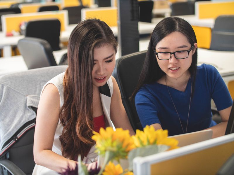 Two women at a desk researching on a laptop.