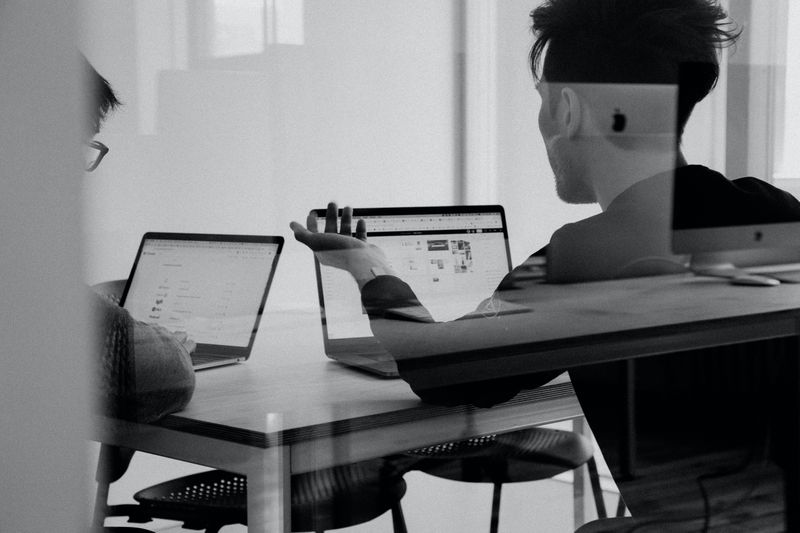 Two web designers discussing their work beside each other on their laptops.