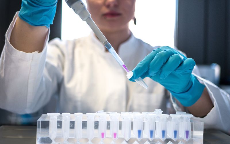 Scientist in protective gear putting a solution into a test tube with a syringe