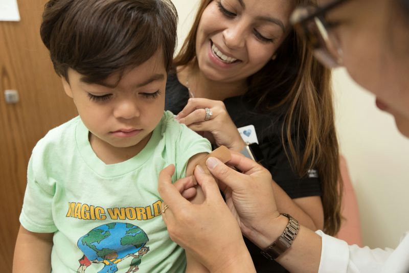 A doctor tending to a young patient with his mom looking on.