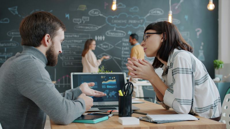 A group of coworkers discussing business at a table and at a chalkboard.