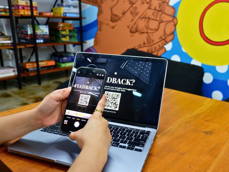 A person holds up a phone to read a QR code on a laptop screen.