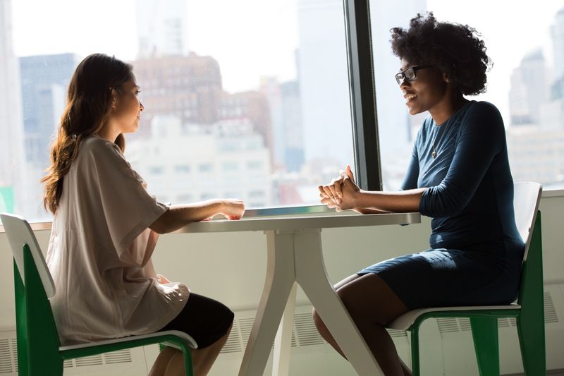 Two women speaking privately at an office table.