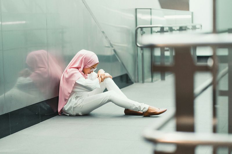 A sad young woman sitting alone on the floor of a school. 