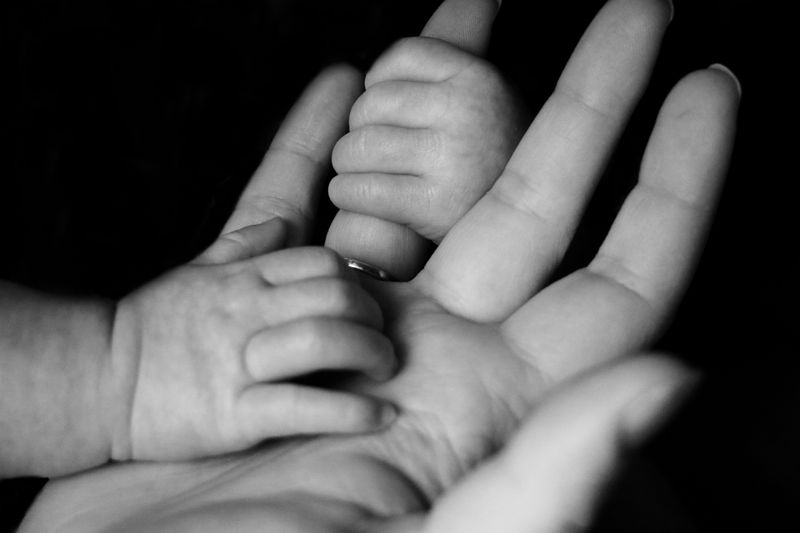 Baby hand on the palm of an adult hand with other baby hand holding on to the adult's finger.