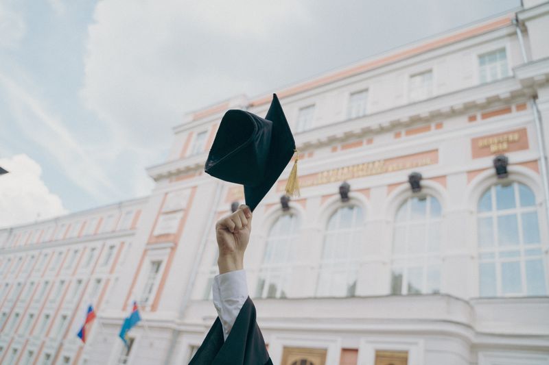 College grad holding college cap up to the air.