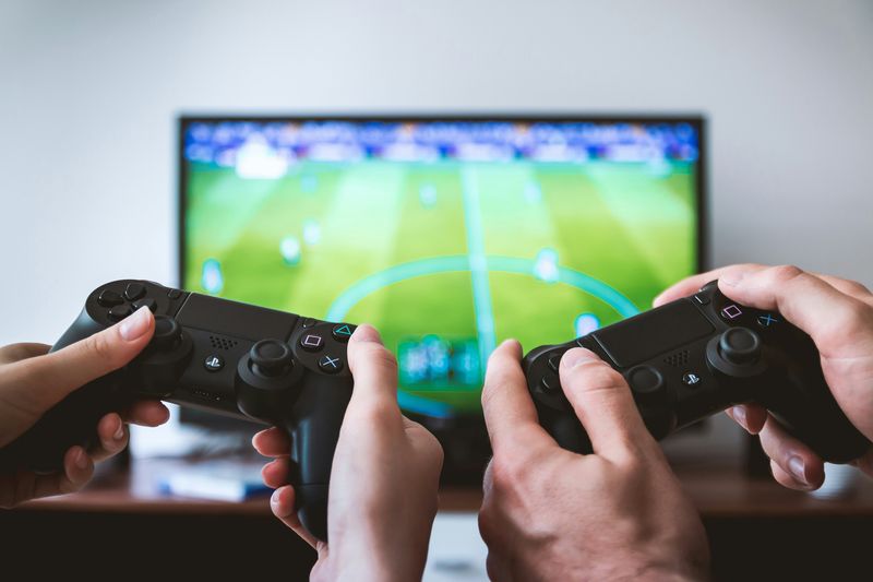 Two different people, each holding a gaming controller and playing video games.