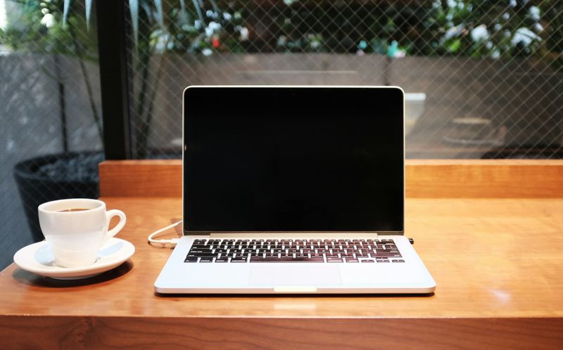 A coffee cup is next to a laptop on a wooden desk. 