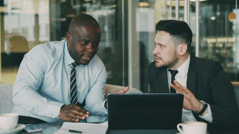 A man speaks with his boss at a desk.