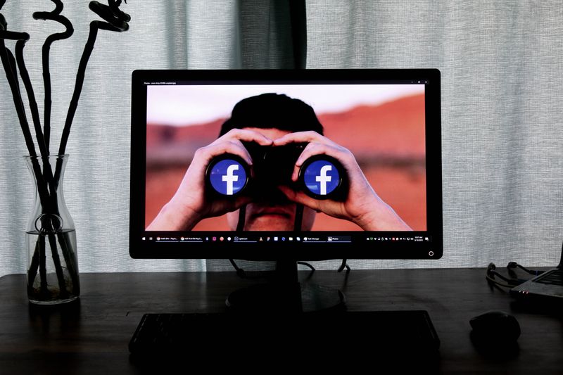 A person seeing through binoculars with facebook logo on the lens. 