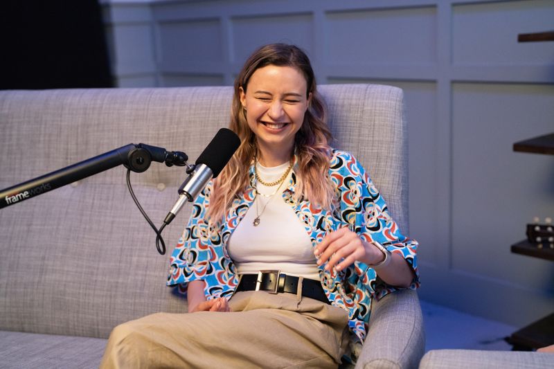 Person on a couch laughing with a microphone.