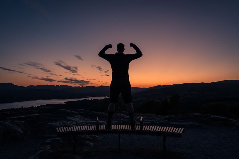 A man flexing from a mountaintop with a beautiful view during sunset.