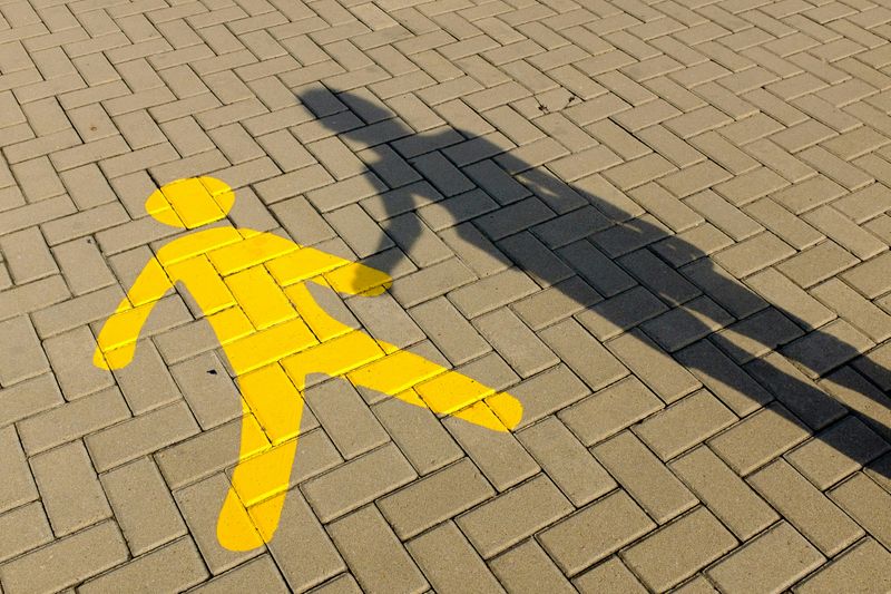 A person's shadow on a brick walkway. The shadow appears to hold the hand of a painted outline of a child.