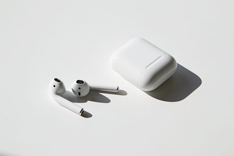 Airpods sit on a blank white space beside their case. 