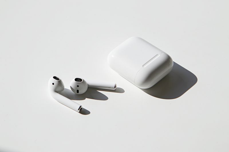 Airpods sit on a blank white space beside their case.