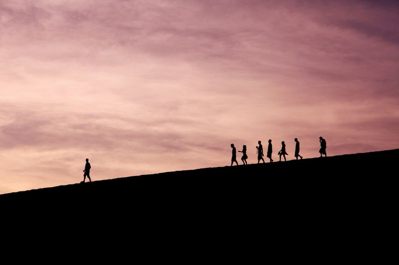 A silhouette of people walking down a hill. One person walks ahead.