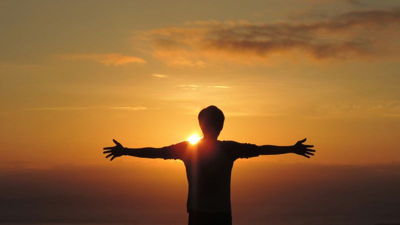 A person with open arms facing the sun.